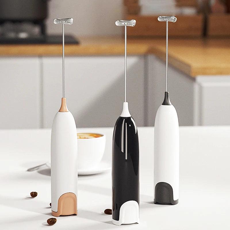 Three milk frothers (white, black, and white with beige base) on a kitchen countertop.