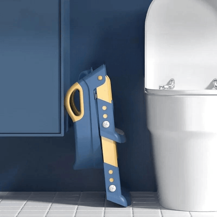 A folded blue and yellow toddler toilet seat with step ladder leaning against a blue bathroom wall beside a white toilet.