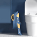 A folded blue and yellow toddler toilet seat with step ladder leaning against a blue bathroom wall beside a white toilet.