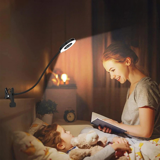 A woman reading to a child in bed, illuminated by the flexible LED ring light clipped to the headboard. The scene shows the light providing focused illumination, creating a cozy atmosphere.