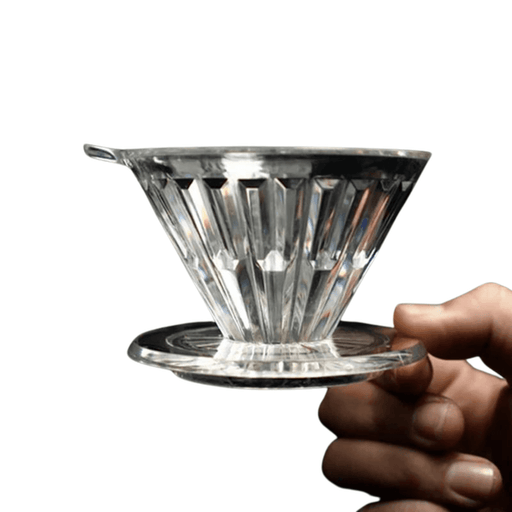 A hand holding a clear Crystal coffee dripper against a white background, showcasing its detailed, ribbed design and sturdy base.