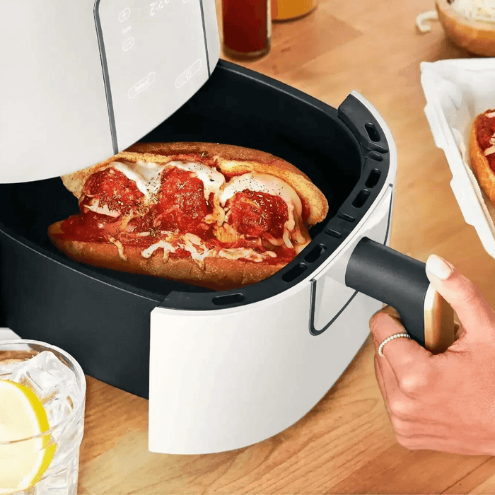 A sandwich being cooked inside an air fryer, with a person holding the air fryer basket handle.