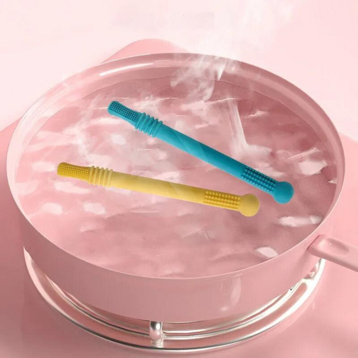 Two silicone teething sticks, one yellow and one blue, are shown in a pink bowl of steaming water, indicating they are being sterilized.