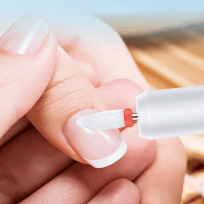 a close-up of a person's nails being shaped with a white nail drill.