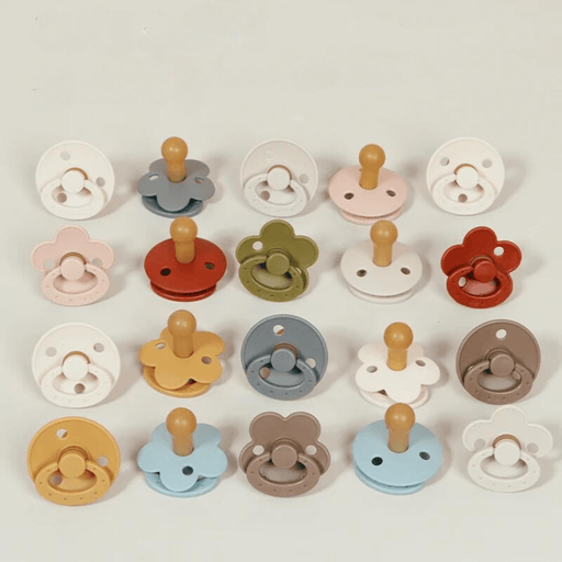 An overhead view of 20 pacifiers arranged in a grid, showcasing different base colors and shapes, including round and flower designs, with each having a bulbous nipple.