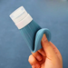 Blue ribbed silicone travel bottle with a flexible loop handle held in a hand, featuring a secure white cap. This portable and reusable bottle is designed for easy carrying and dispensing of liquids like shampoo or lotion, ideal for travel and daily use.