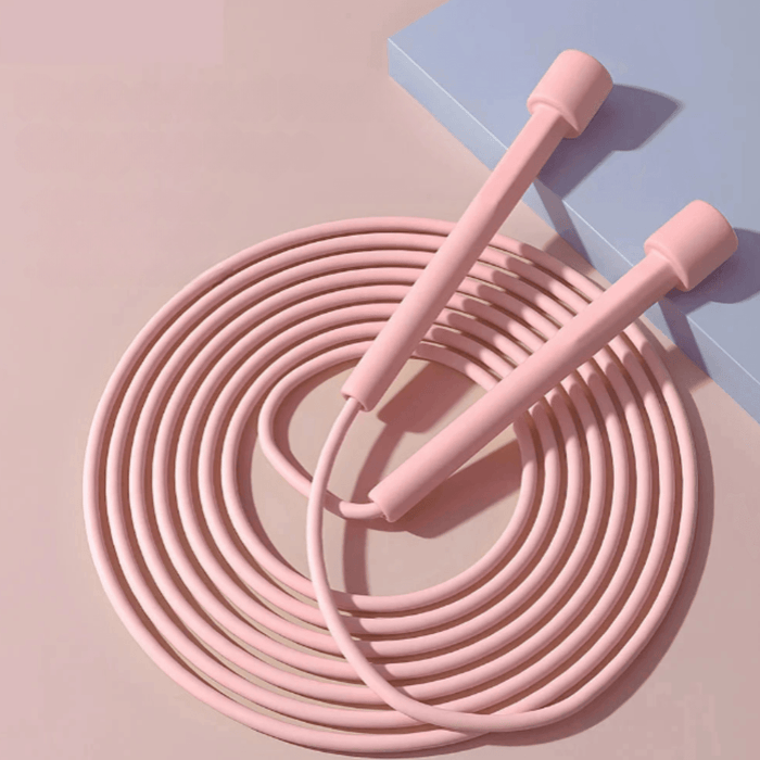 A neatly coiled pink jump rope with long, cylindrical handles placed on a soft pink surface, showcasing its lightweight and flexible design.