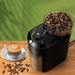 The grinder is shown on a wooden countertop next to a cup of cappuccino. Coffee beans are scattered around, highlighting its use for making espresso drinks.