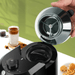 A close-up view of the grinder with its lid open, showing the internal blades. It’s placed beside a glass of iced coffee and some cookies.