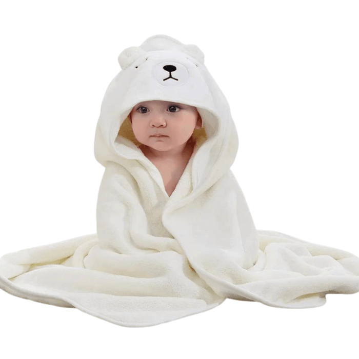 A baby wrapped in a white hooded towel designed to look like a bear. The hood features an embroidered bear face with ears. The baby is sitting with the towel draped around them, looking snug and warm.