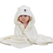 A baby wrapped in a white hooded towel designed to look like a bear. The hood features an embroidered bear face with ears. The baby is sitting with the towel draped around them, looking snug and warm.