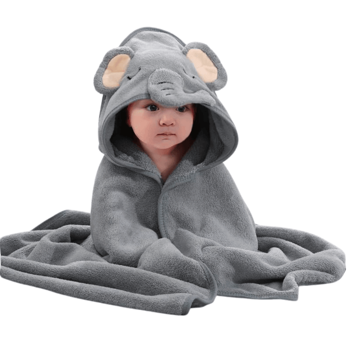 A baby wrapped in a grey hooded towel designed to look like an elephant. The towel has an elephant face on the hood with floppy ears and a trunk. The baby is sitting with the towel wrapped around them, looking comfortable and cozy.