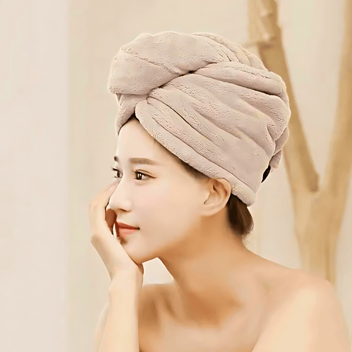 A woman with a beige towel wrapped around her head in a turban style. She has a serene expression, and the towel looks plush and comfortable.