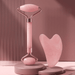 Pink Gua Sha and face roller diplayed on pink background, and standing on two stages.