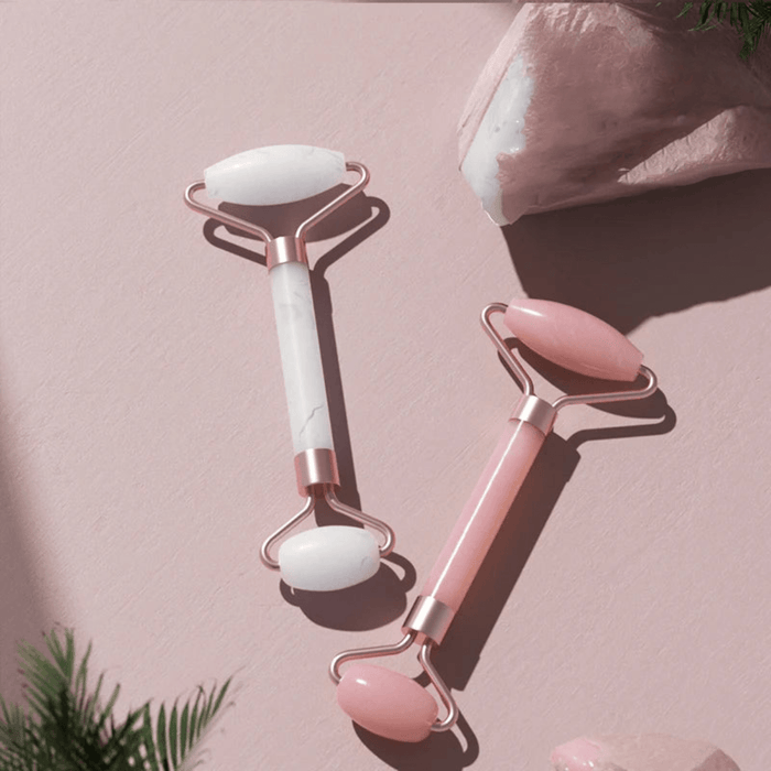 A white and pink jade facial rollers for skincare routines display on pink background.