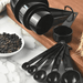 The image shows both the measuring cups and spoons together, arranged on a kitchen countertop. The set is placed near a small bowl of black peppercorns, providing a sense of scale and suggesting their use in cooking.