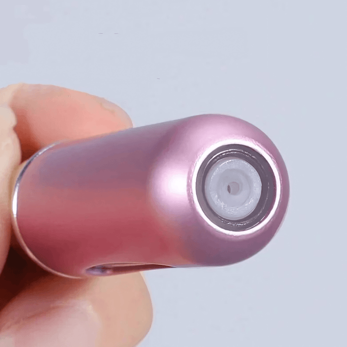 A close-up of the bottom of a pink portable perfume spray bottle, focusing on the refill valve.