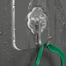 The hook is shown attached to a wet surface, demonstrating its water resistance. A green object is hanging from the hook, illustrating its holding capability even in moist conditions.