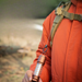 A person wearing an orange jacket with a retractable tool attached to their backpack strap.