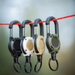 Four retractable tools in different colors (black, white, beige, and green) hanging on a red cord.