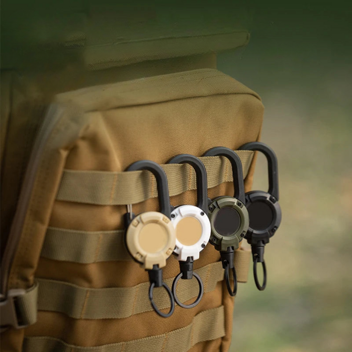 Four retractable tools in beige, white, green, and black attached to the molle webbing on a tan backpack.