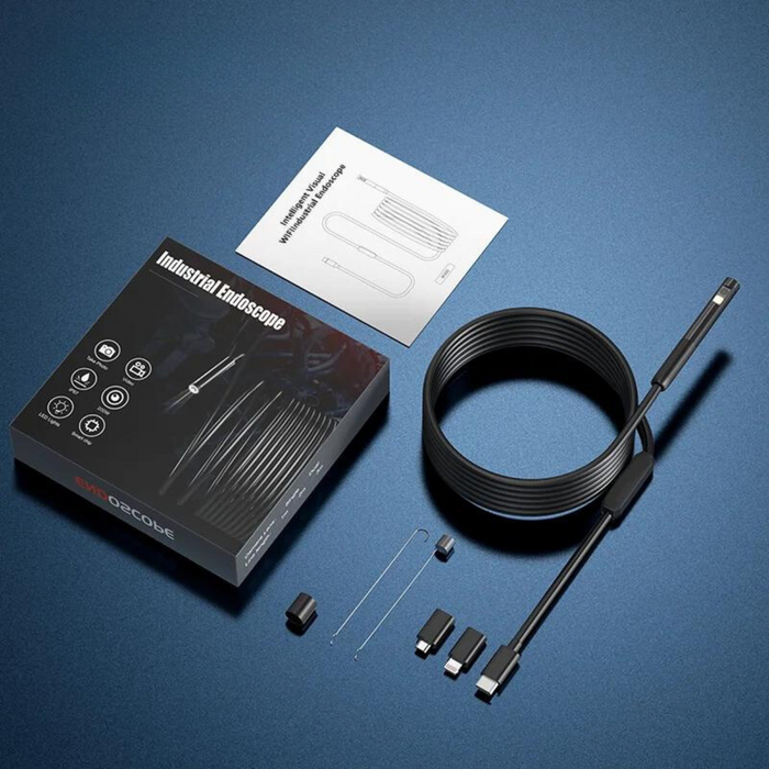 Industrial endoscope kit laid out on a dark blue surface, including the camera, a long coiled cable, various adapters, and an instruction manual.