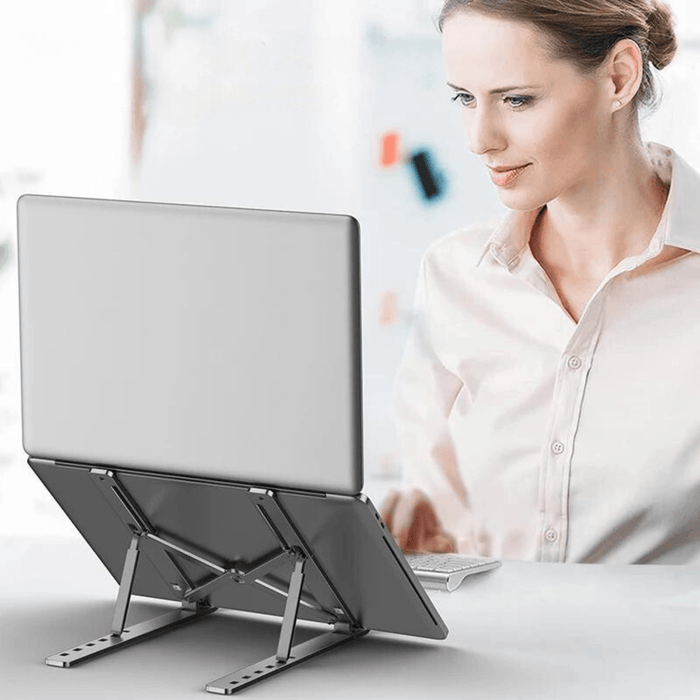 Woman using a laptop on a silver adjustable stand, enhancing her ergonomic posture.