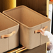 An empty beige fabric storage bin with orange handles, placed inside a closet. A person is seen holding the handle of the bin, indicating that it can be easily pulled out and moved. The bin is labeled with "Fashion."