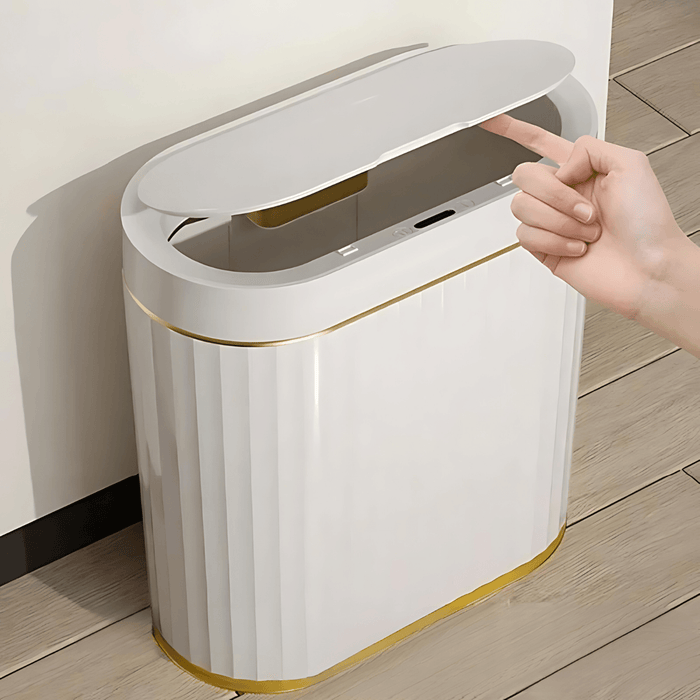 A stylish modern trash can with a touchless lid operation, shown in a minimalist design. The can features vertical ridges and is accented with a gold base and trim. A person's hand is seen activating the lid mechanism by touching a button, demonstrating the ease and hygiene of the touchless feature.