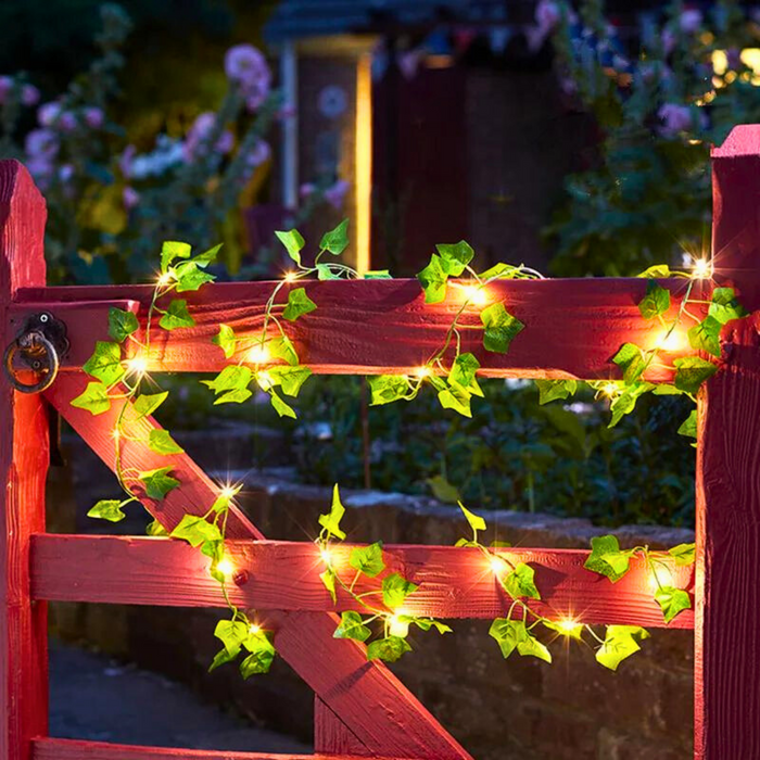 A charming red wooden garden gate adorned with green ivy leaves and fairy lights, casting a magical glow that enhances the entrance's rustic beauty. This setting creates a welcoming and enchanting atmosphere, ideal for garden pathways or entrances.