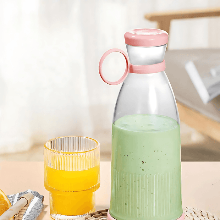 The pink portable blender filled with a green smoothie next to a glass of orange juice, demonstrating its use.