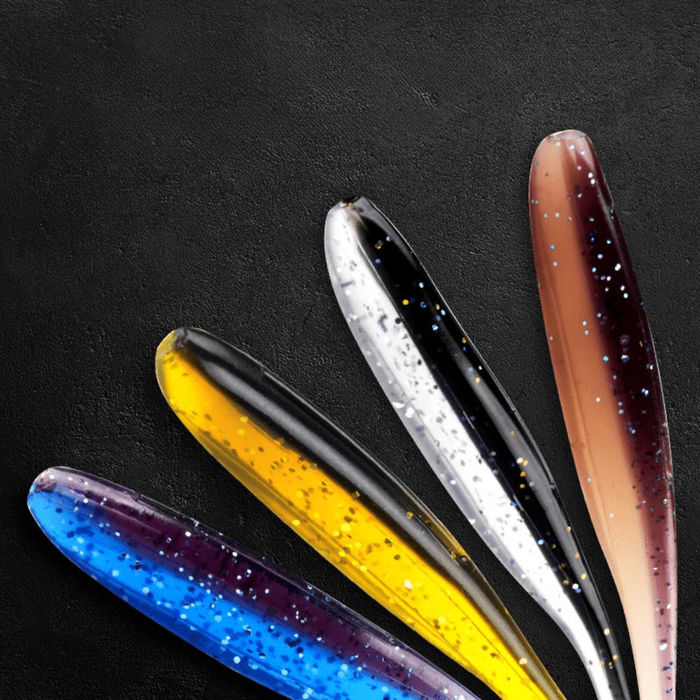 A close-up view of five soft plastic fishing lures, fanned out on a dark background, featuring different color patterns, including blue, yellow, white, and brown, with speckled designs.