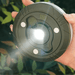 A person holding a round, black multifunction camping light with a bright white LED in the center.