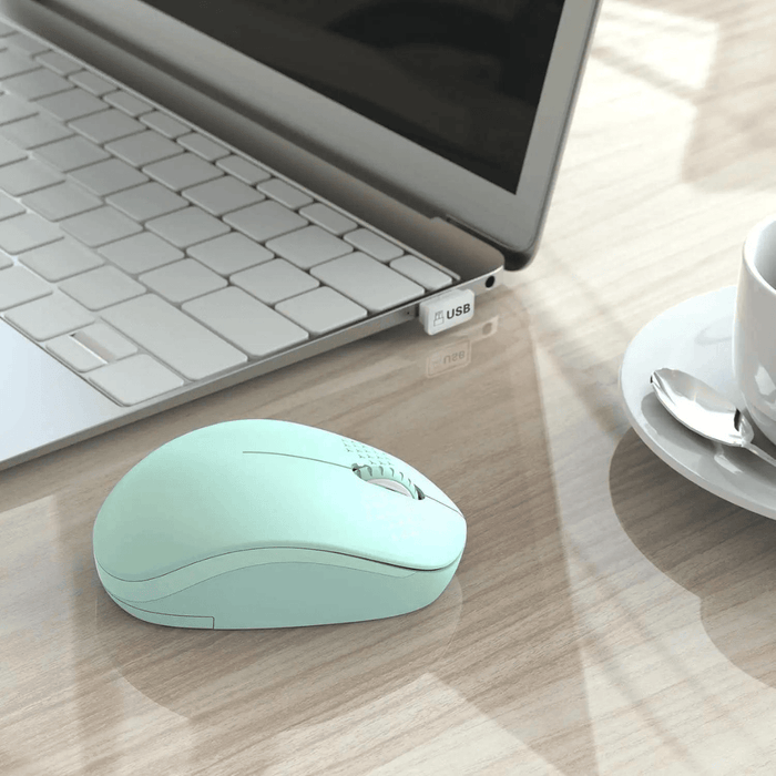 A mint green wireless mouse placed next to a laptop with a USB receiver plugged in, displayed on a wooden table background with a cup and saucer in the background.