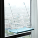 A blue version of the window-mounted cat hammock installed on a window, overlooking a cityscape.