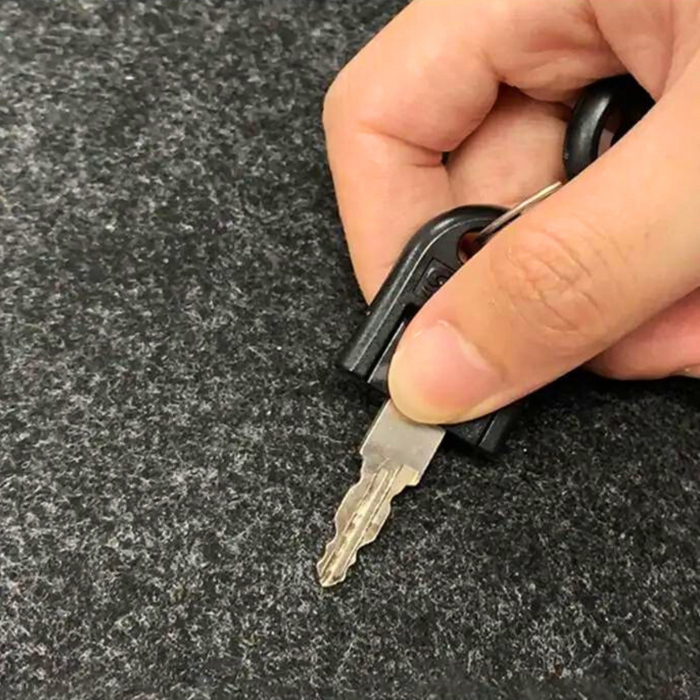 A close-up of a hand holding a key on a textured grey surface, demonstrating the durability and scratch resistance of the PC desk pad material.