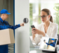 A delivery person using a video doorbell, viewed by a woman on her smartphone.