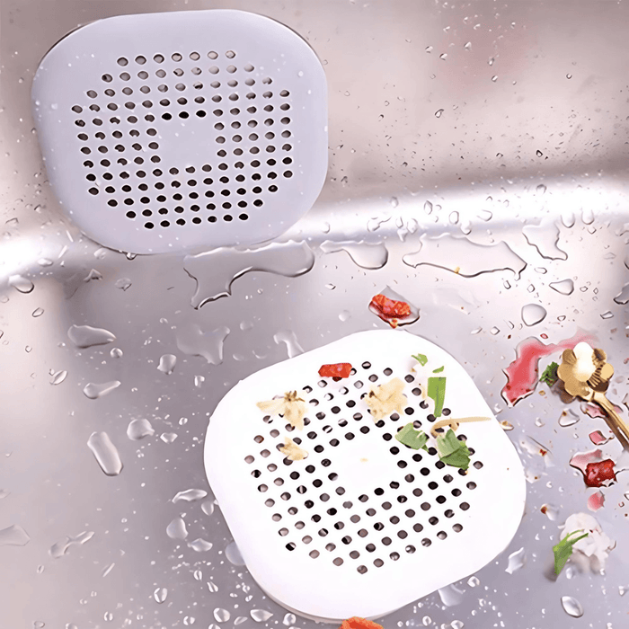 Two gray and white silicone sink strainers with food debris in a kitchen sink.