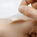 A close-up of a transparent adhesive bandage being peeled away from the back of the hand, demonstrating its flexibility and the ease with which it can be applied to the skin.