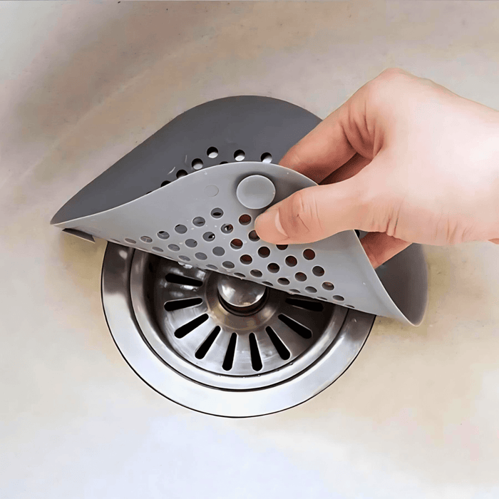 Hand lifting a gray silicone sink strainer from a sink drain.