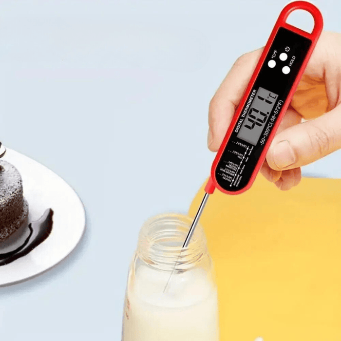 A hand holding a digital thermometer measuring the temperature of milk in a bottle.