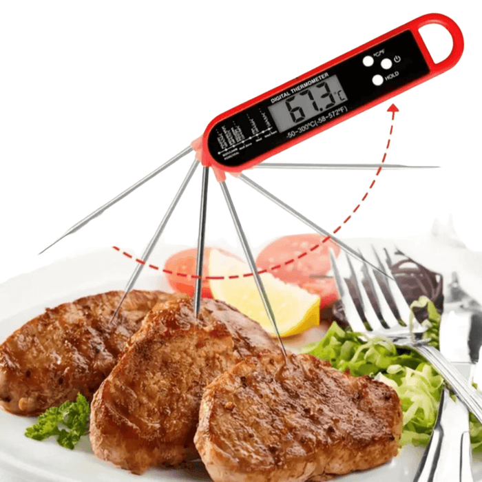 A digital thermometer with a red casing, showing its probe measuring the temperature of grilled meat on a plate.