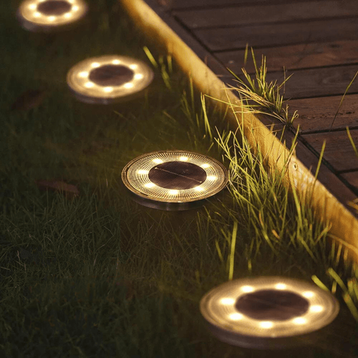 Four solar garden lights installed in the grass beside a wooden deck, shining brightly at night and casting a warm light on the ground.