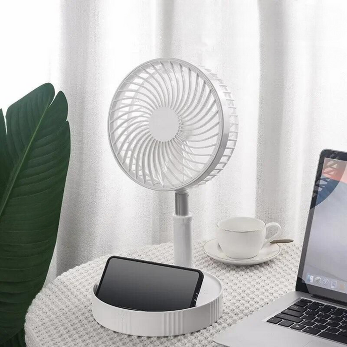 Compact white fan on a desk with a plant, cup, phone, and laptop.