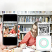 A person holds a smartphone displaying a photo being printed by a small white printer. In the background, two girls are studying in a library.