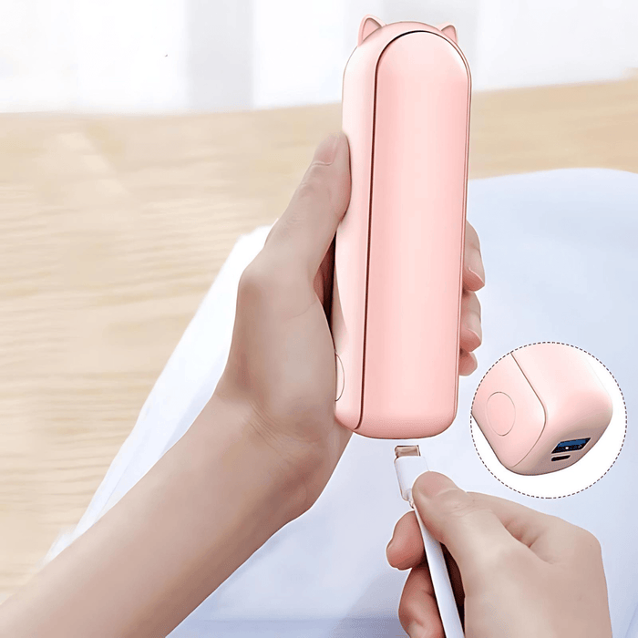 A person holding a pink portable handheld fan being charged via a USB cable. A close-up inset highlights the USB port on the fan, which is designed for convenient charging. Additionally, the image displays the fan shut and compact, emphasizing its sleek and minimalist design.