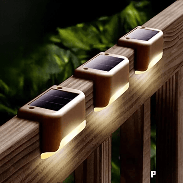 A series of small, brown rectangular solar lights mounted on a wooden deck railing, providing ambient lighting.