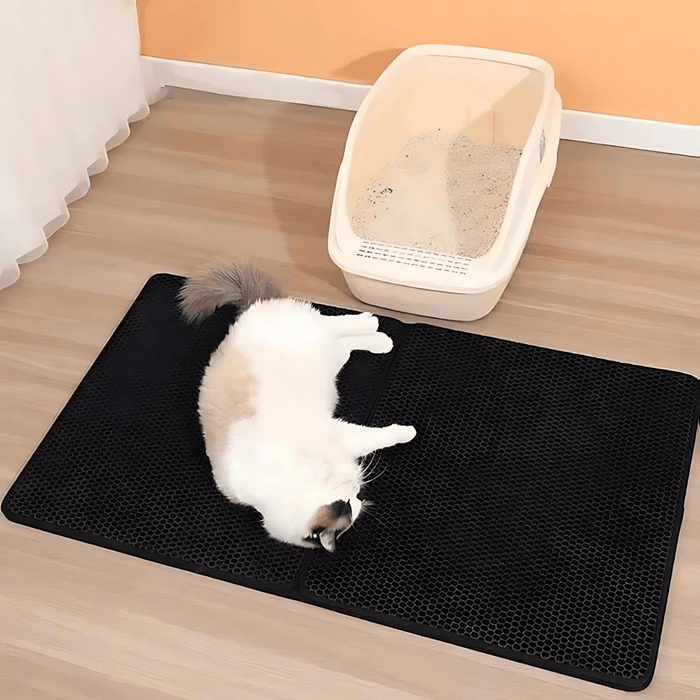 A cat lying on the mat beside its litter box, demonstrating the mat's practical use in a home setting.