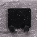 A black wall-mounted holder with two hooks, adhered to a wet, textured surface with water droplets scattered around.