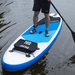 A person standing on a blue and white paddleboard with a black storage bag attached at the front.